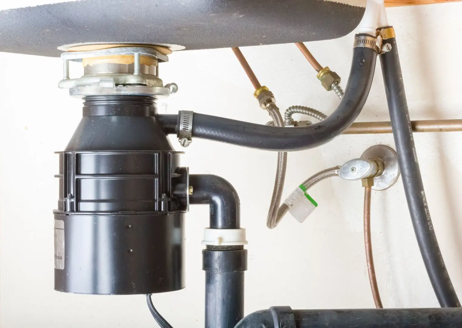 A garbage disposal unit installed under a kitchen sink with connected pipes and plumbing lines visible.