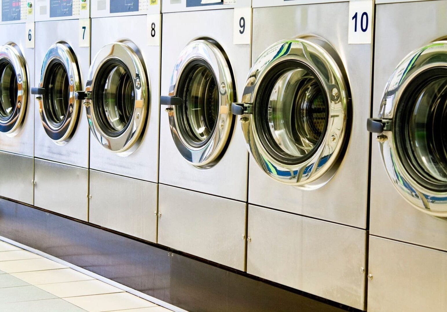 A row of front-loading washing machines in a laundromat, each with a numbered label above the door.